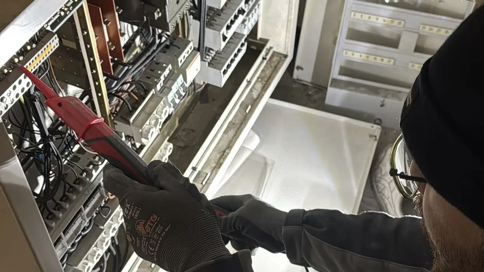 Elektriker kniet vor einer geöffneten Unterverteilung und prüft sie mit einem roten Spannungsprüfer